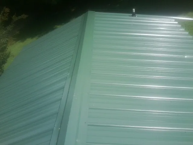 New green metal panels meeting at the ridge of a roof — Flat Roof Repair work by our crew in Conrad